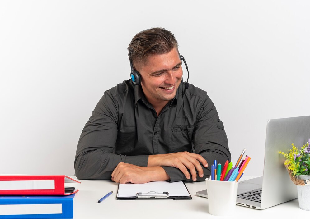 joven sonriente rubia oficinista hombre auriculares sienta escritorio herramientas oficina mirando portatil aislado sobre fondo blanco espacio copia 141793 65470